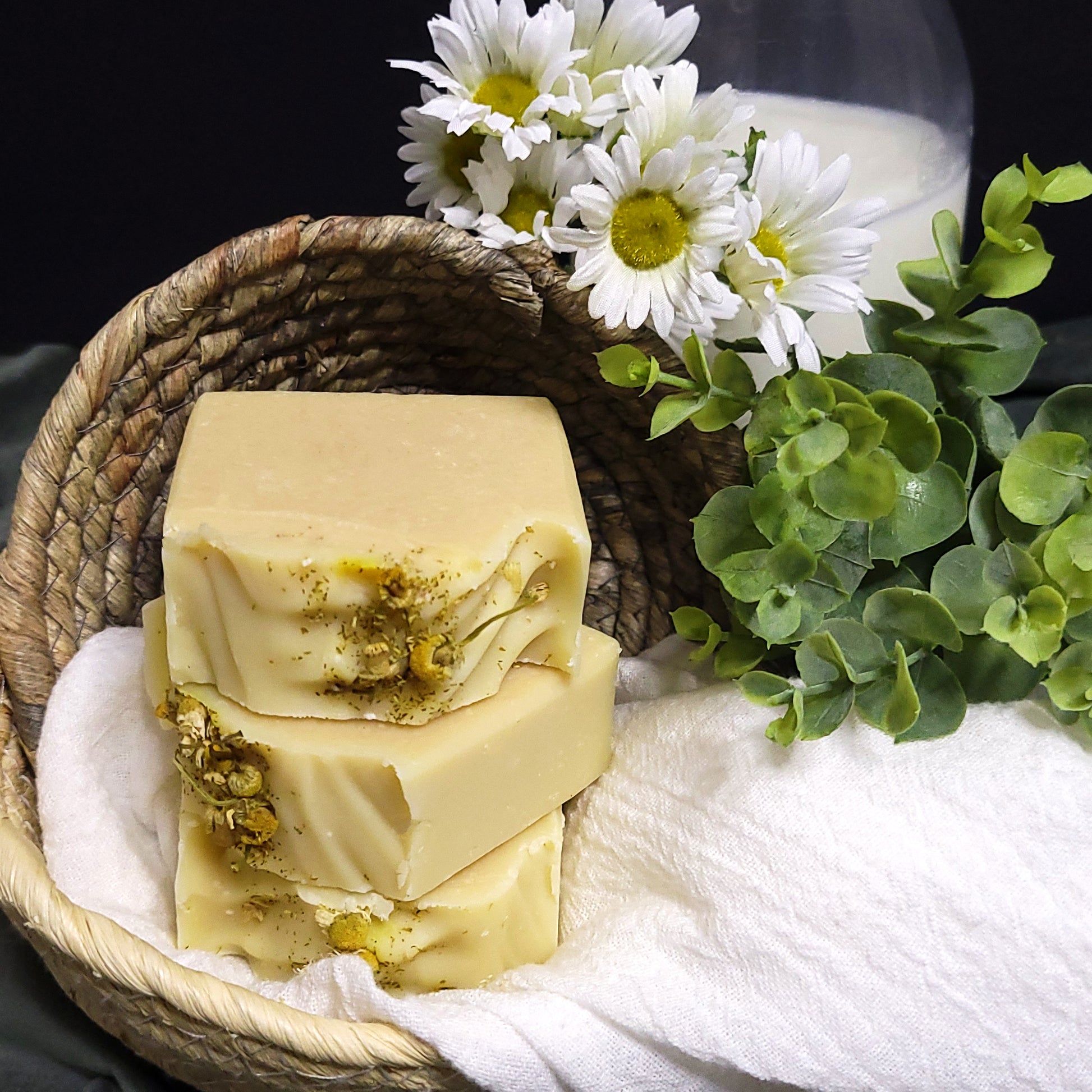 Stack of natural soap bars with greenery, goat milk, and flowers on a white towel.